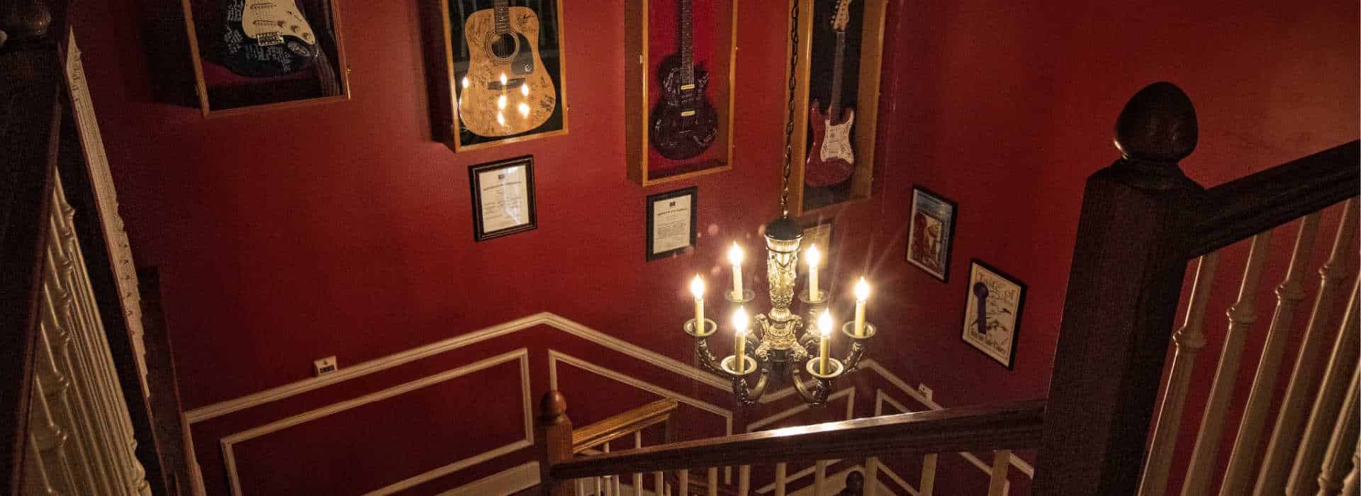 guitars on the wall with a lighted chandelier in the foreground