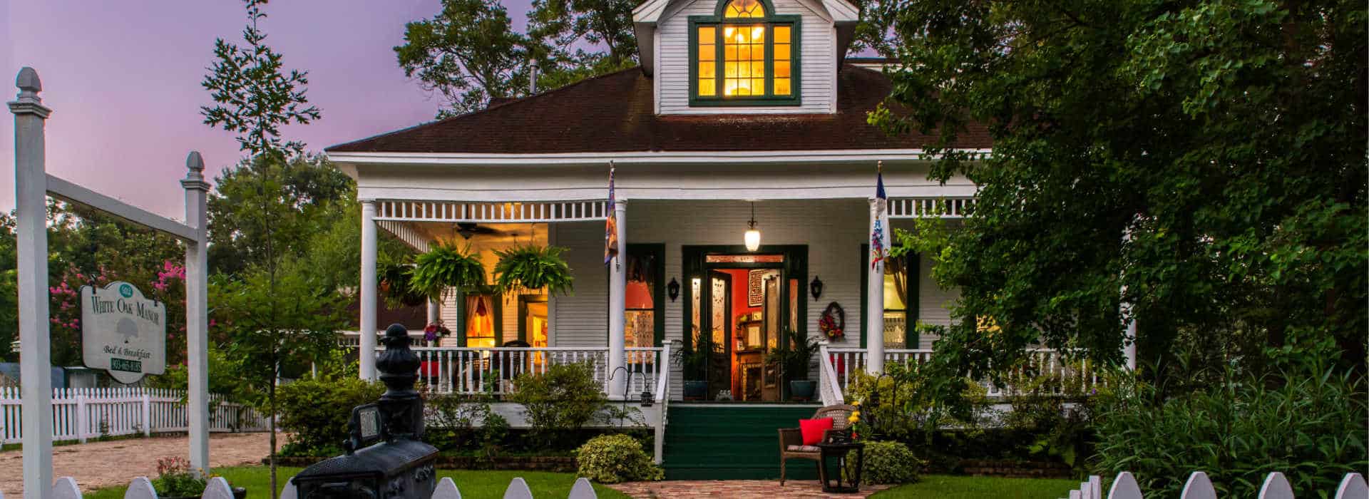 green yard with a white house with the room lights on at dusk