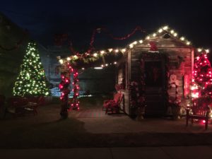 decorated green Christmas tree next to an old wooden building decorated with red and white lights 