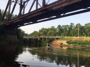 people in a blue kayak on the river surrounded on the banks with leafy trees and some sandy beachs