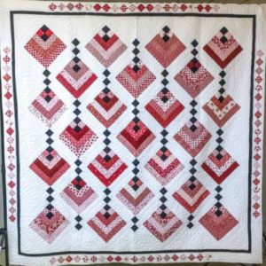 q white quilt with squares of red, pink,rose and black colors in rows.