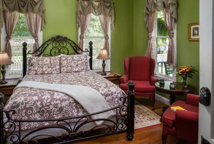iron bed with dusty purple quilt and two burgundy chairs
