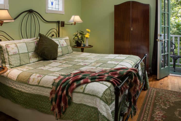 large bed with green and white spread in front of a wooden cupboard