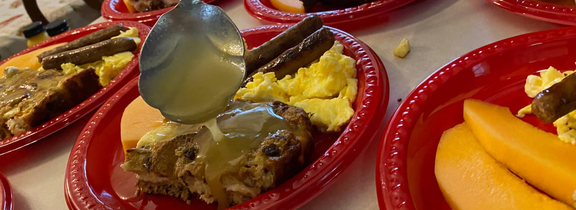 red plate with eggs sausage bread pudding with a spoon pouring sauce over it