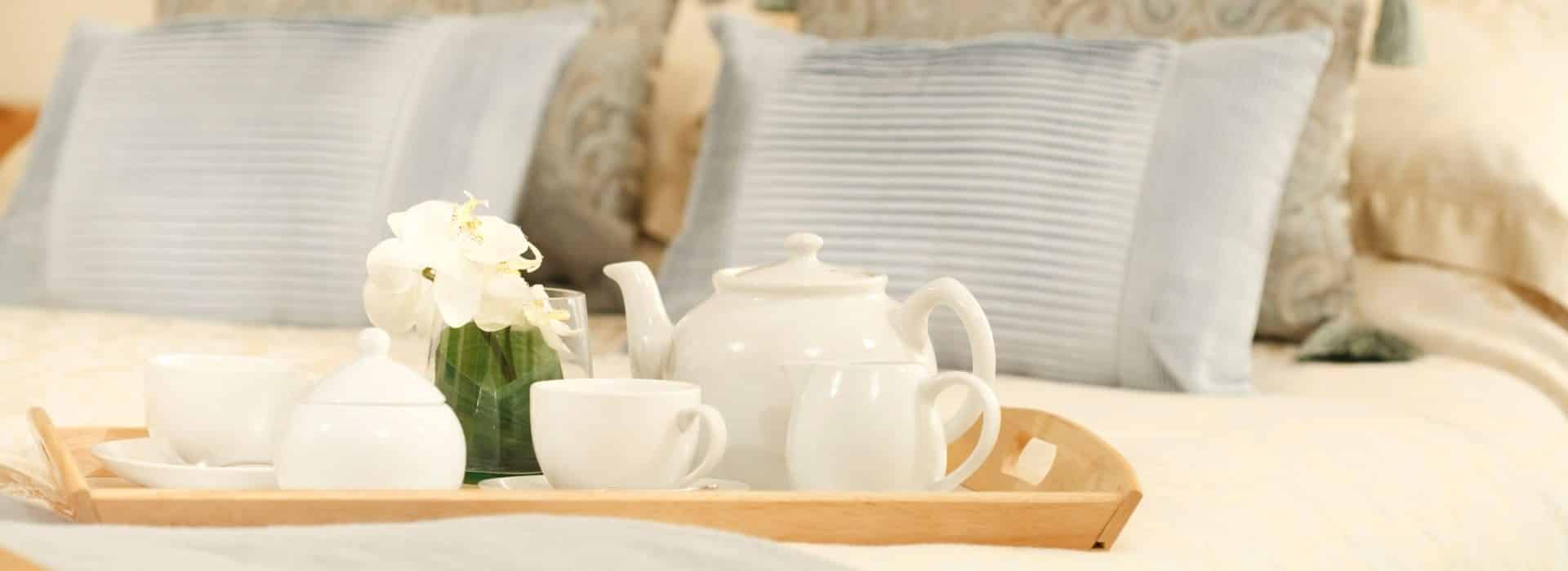 Wooden tray with white tea set on top of bed