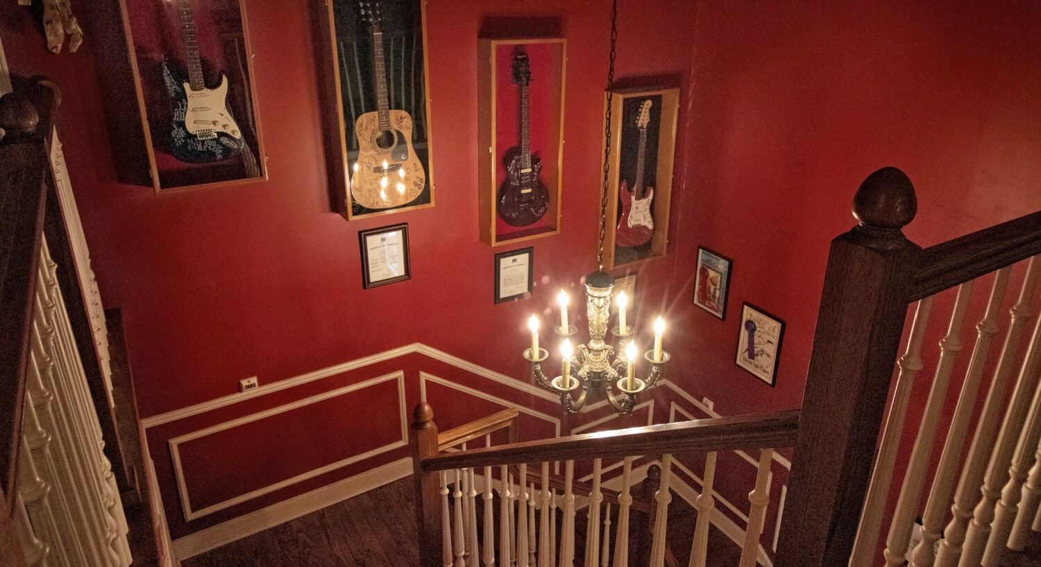 Dark wooden staircase with burgundy walls and vanilla trim and four wooden display cases with signed guitars hanging on the wall