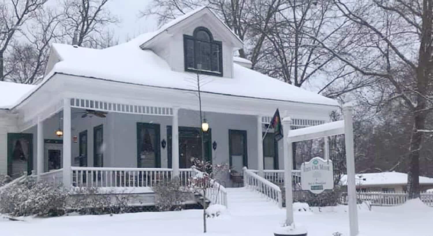 Exterior view of the property covered in snow surrounded by trees and bushes with no leaves