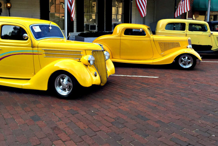 3 old cars painted in bright yellow on the red brick streets